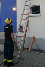 Doppelte Sicherung einer Leiter durch Fußpunktsicherung eines Helfers und Mittelpunktsicherung mittels Leinenverbindung sowie Verankerung im Fenster.